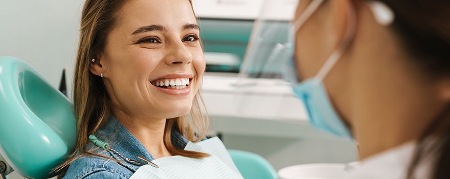 Junge Frau sitzt lächelnd im Zahnarztstuhl und bekommt eine professionelle Mundhygiene
