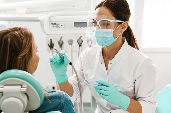 Junge Frau sitzt im Zahnarztstuhl und bekommt eine professionelle Mundhygiene von einer Zahnärztin