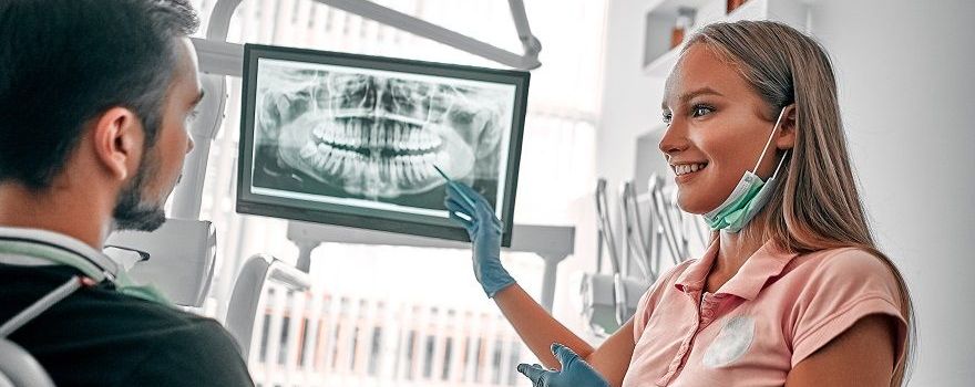 Ein Mann sitzt bei der Zahnärztin, schaut auf ein Röntgenbild seiner Zähne und wird zum Thema Zahnkrone beraten