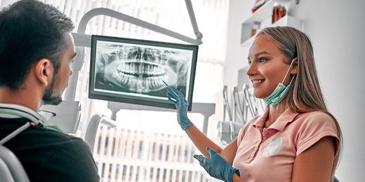 Ein Mann sitzt bei der Zahnärztin, schaut auf ein Röntgenbild seiner Zähne und wird zum Thema Zahnkrone beraten