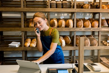 Bäckereifachverkäuferin tippt auf Tablet und telefoniert