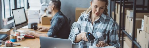 Frau im stylischen Flanellhemd scannt einen Barcode in der Versandabteilung
