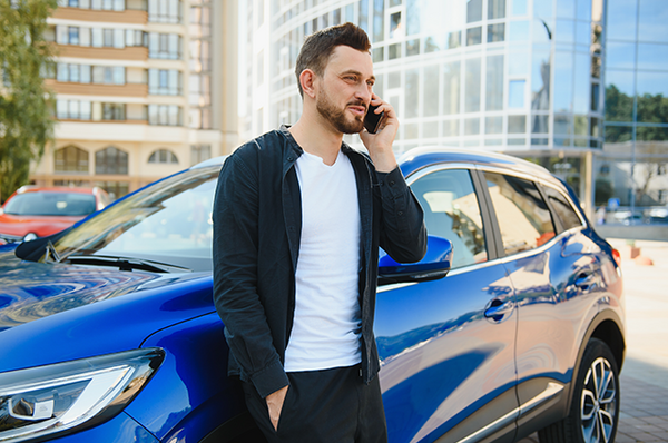 Mann telefoniert vor einem blauen Auto mit der Versicherung.