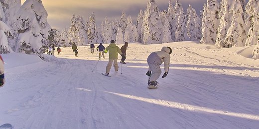 Snowboarder und Skifahrer auf einer verschneiten idyllischen Piste mit tiefstehender Sonne