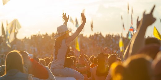 Frau sitzt auf den Schultern eines Mannes und jubelt bei einem Musikfestival