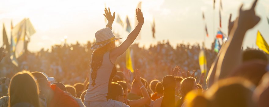 Frau sitzt auf den Schultern eines Mannes und jubelt bei einem Musikfestival