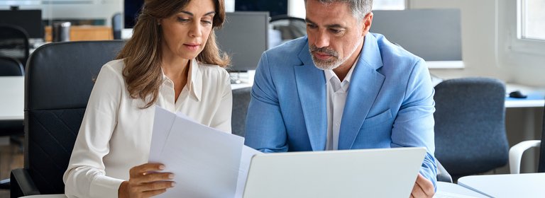 Zwei Personen sitzen im Büro am Laptop und Besprechen eine Unterlage