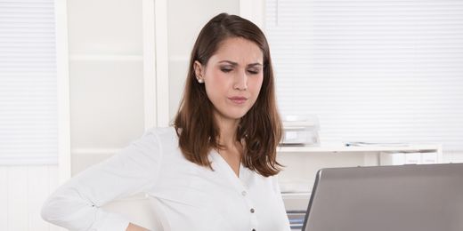 Frau sitzt mit Rückenschmerzen beim Laptop