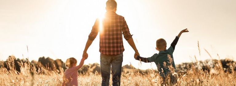 Mann geht mit zwei Kindern an der Hand über ein Feld