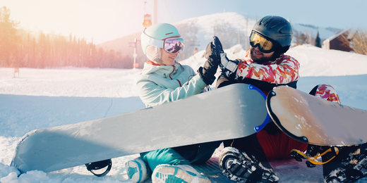 Zwei Snowboarder sitzen im Schnee und geben sich ein High-Five