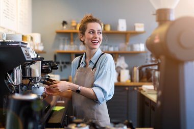 Barista steht vor Kaffeemaschine und lächelt