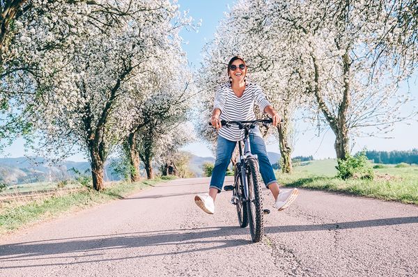 Frau fährt mit Fahrrad durch Allee mit blühenden Bäumen
