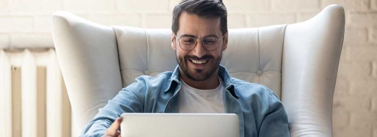 Mann sitzt mit Laptop in einem Couchsessel