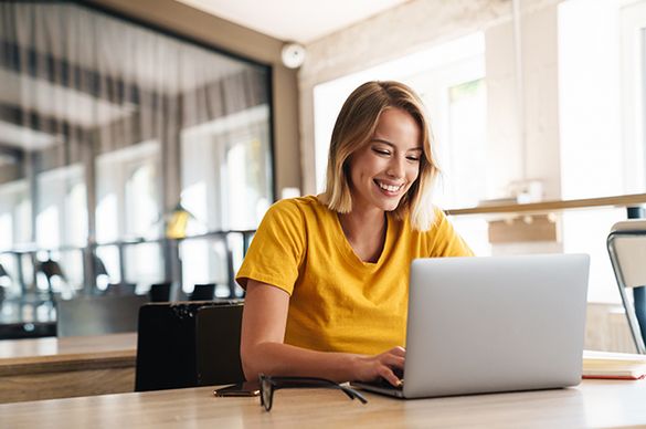 Junge Frau mit gelbem T-Shirt sitzt an Laptop und füllt ein Kontaktformular aus