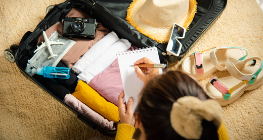 Frau packt ihren Koffer für den Urlaub und schreibt eine Urlaubs-Checkliste