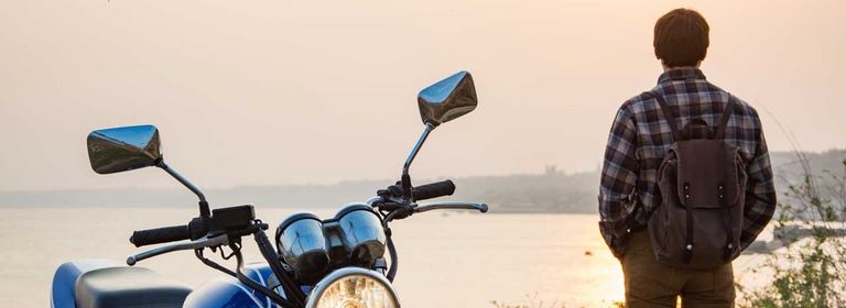 Mann steht neben Motorrad und und schaut aufs Meer