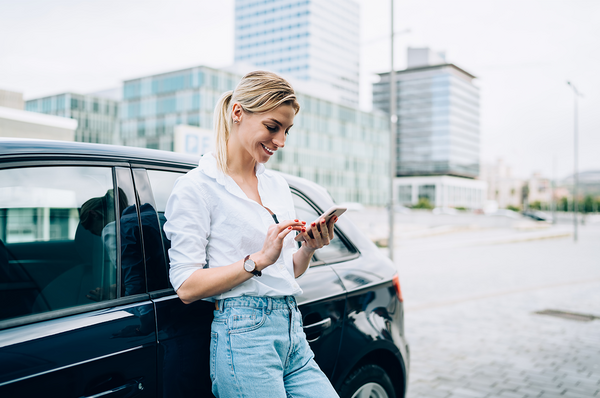 Frau mit einem Smartphone in der Hand lehnt an Auto