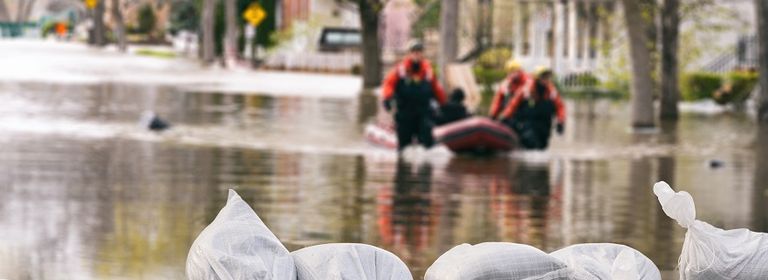 Überschwemmte Straße, durch die Feuerwehrmänner nach Katastropheneinsatz mit Schlauchboot durchs Wasser gehen. 