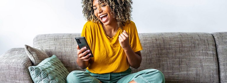 Junge Frau sitzt am Sofa mit Smartphone