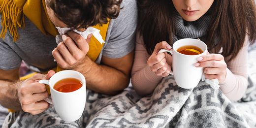 Erkältetes Pärchen sitzt mit Tee und Decke auf der Couch