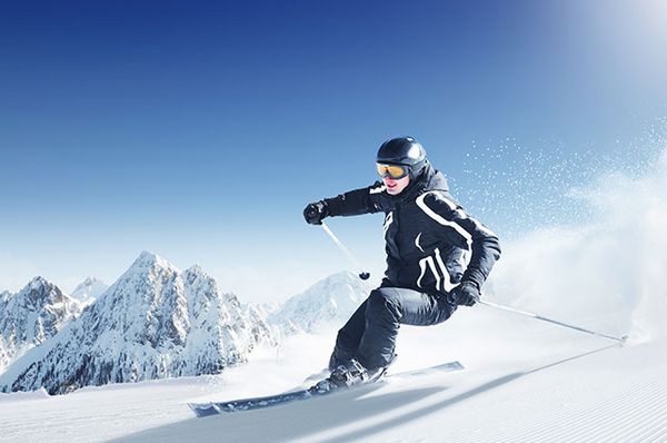 Skifahrer ist mit Skihelm und Skibrille auf einer Piste unterwegs