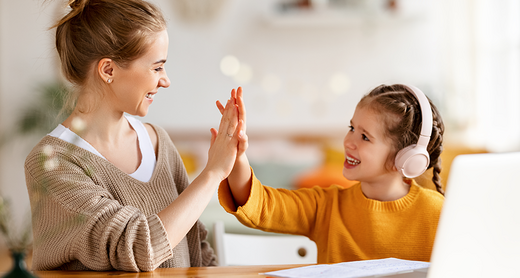 Mutter und Tochter geben sich ein High-Five während das Mädchen ihre Hausaufgaben macht