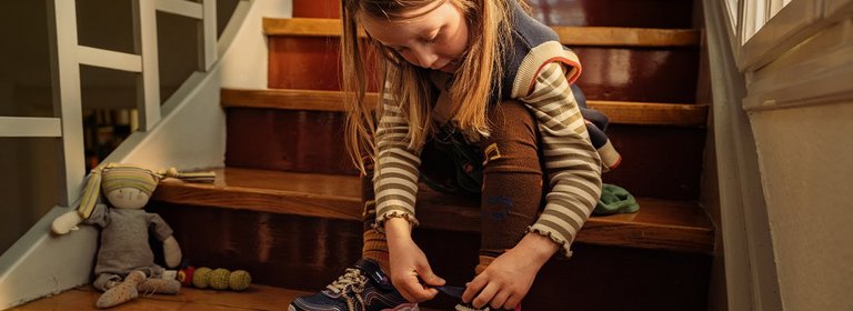 Kind sitzt auf Stufen und bindet sich ihre Schuhe
